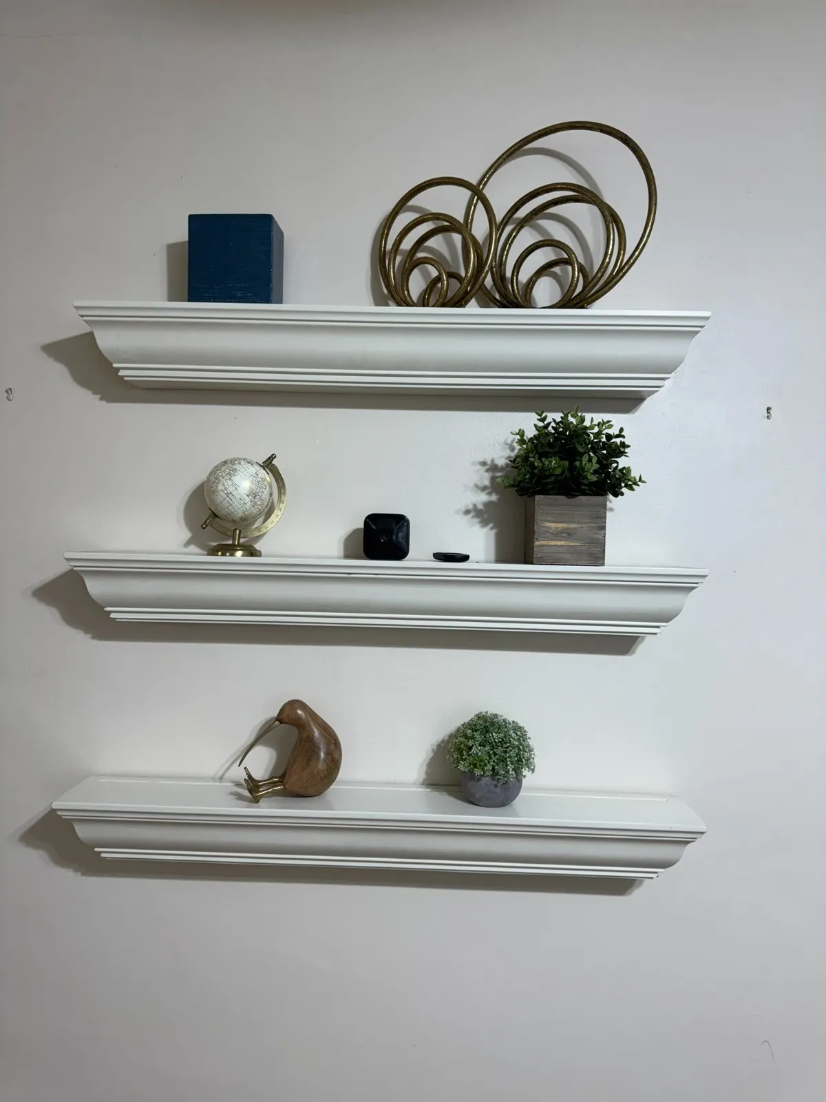 Styling detail by Kultur & Decor: styling detail: floating shelves with globe, gold-ring sculpture, wood bird, potted greenery.