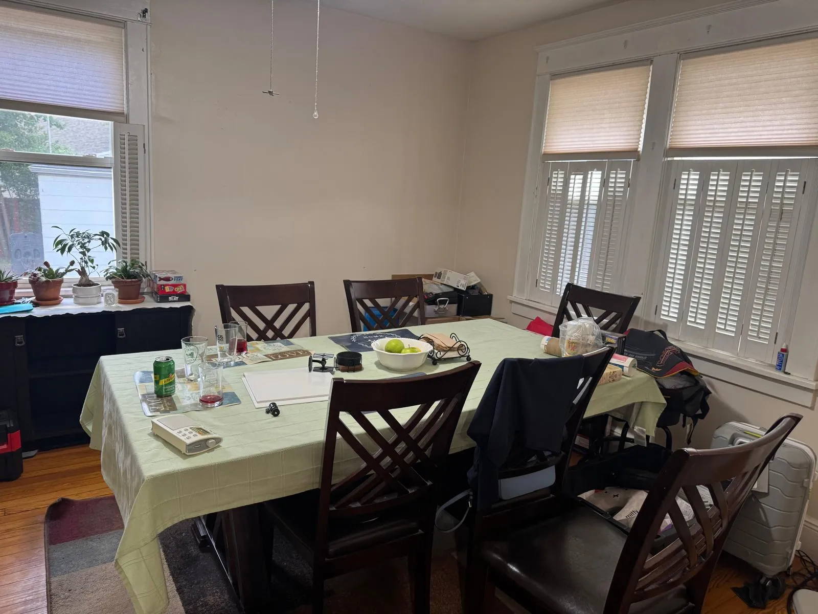 Dining room before restyling: dining before: green cloth, glassware, luggage and bags on chairs.