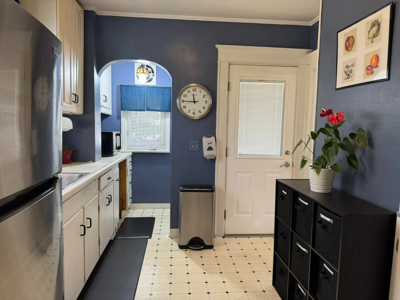 Kitchen after restyling by Kultur & Decor: galley kitchen (navy walls): framed fruit prints, anthurium, storage cubbies (cleanest kitchen angle).