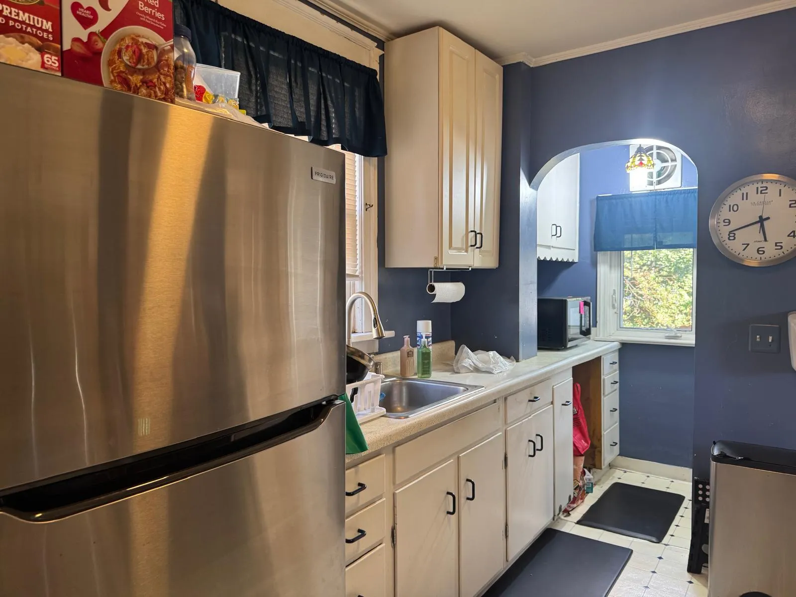 Kitchen before restyling: kitchen before: boxes on fridge, dish soap, plastic bag on counter.