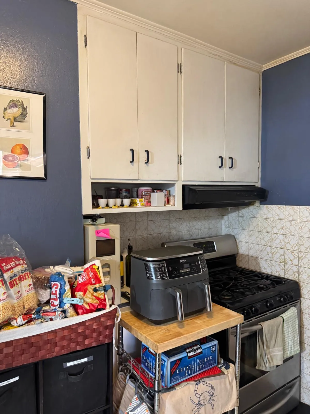 Kitchen before restyling: kitchen before: snack basket, air fryer, cutlery box by stove.