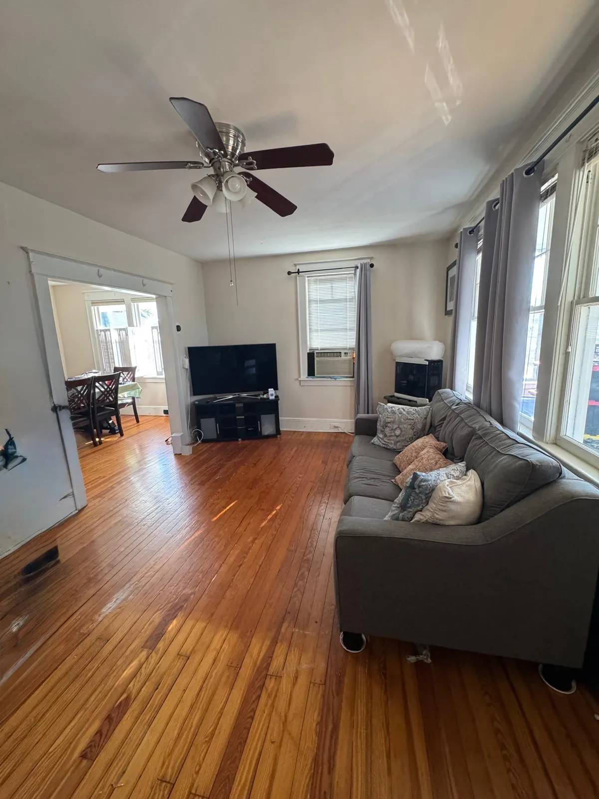 Living room before restyling: living room before, wide: owner's sofa, TV stand, plastic-wrapped PC tower; opens to dining.