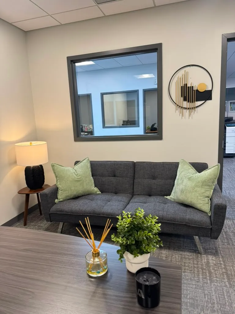 Office after restyling by Kultur & Decor: styled lounge nook: gray loveseat, green pillows, gold wall art, lamp (portrait hero).