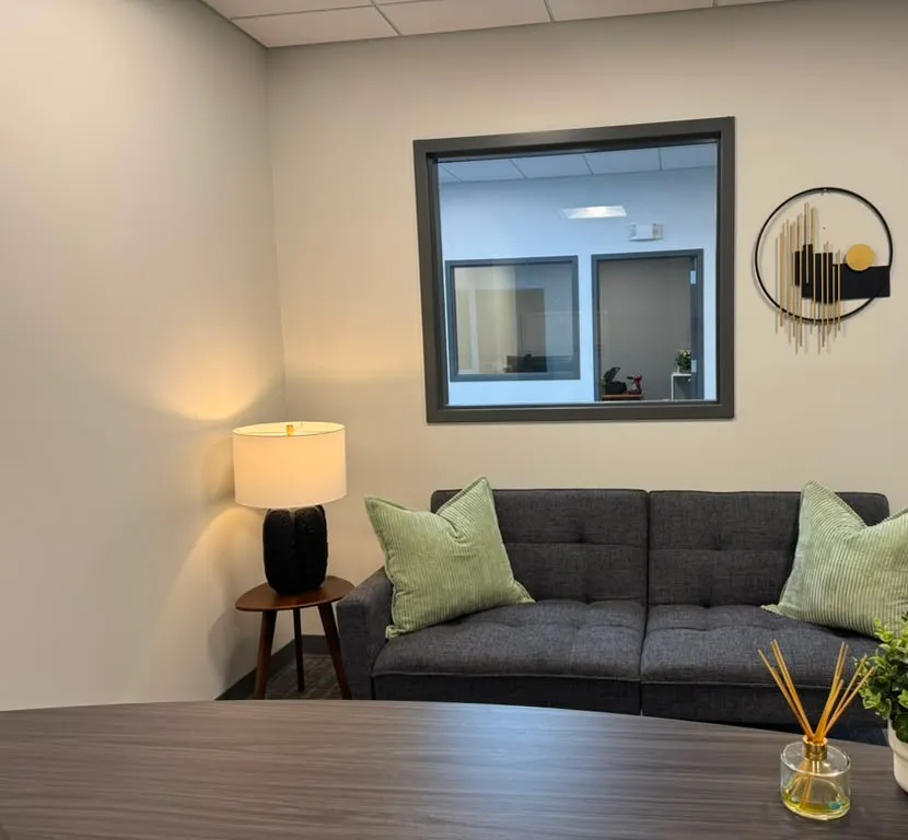 Office after restyling by Kultur & Decor: styled lounge nook, wider landscape; interior window. Cropped right side to exclude the open doorway/hallway with a sliver of the client's logo wall; circular wall art kept in frame, cut at the door frame.