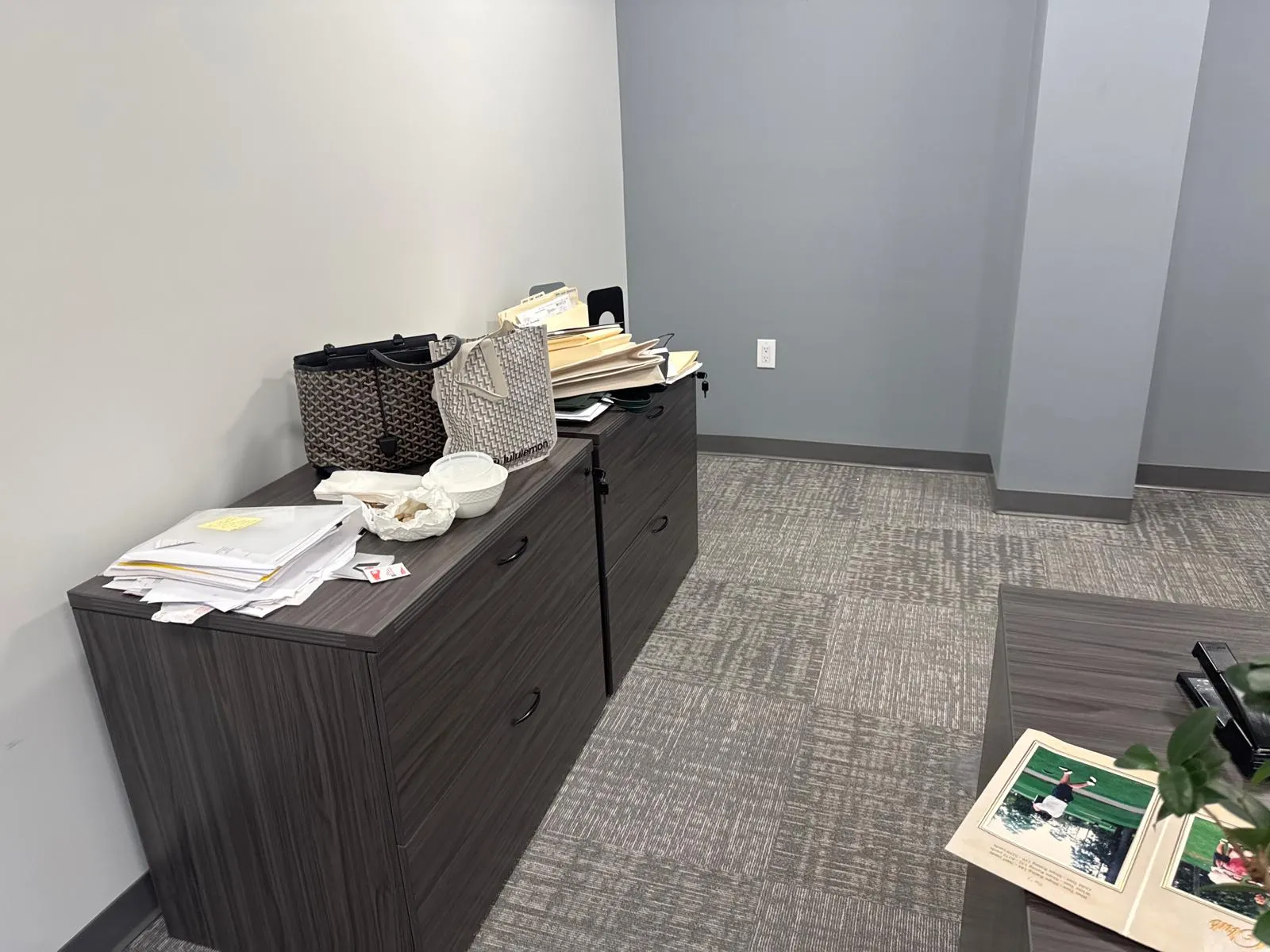Office before restyling: credenza with designer bags and loose papers; bare gray wall.