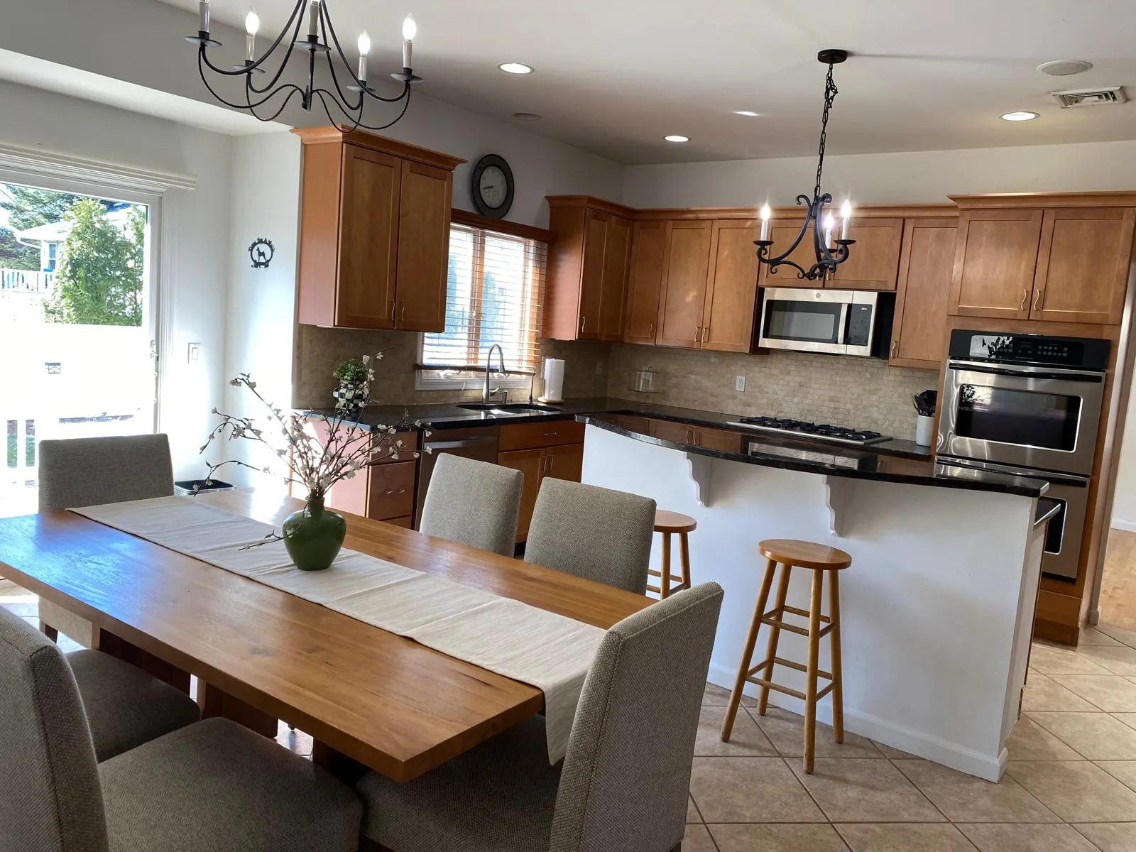 Kitchen/dining room after restyling by Kultur & Decor: counters cleared, stools tucked, table dressed with a linen runner and a green vase of white blossom.