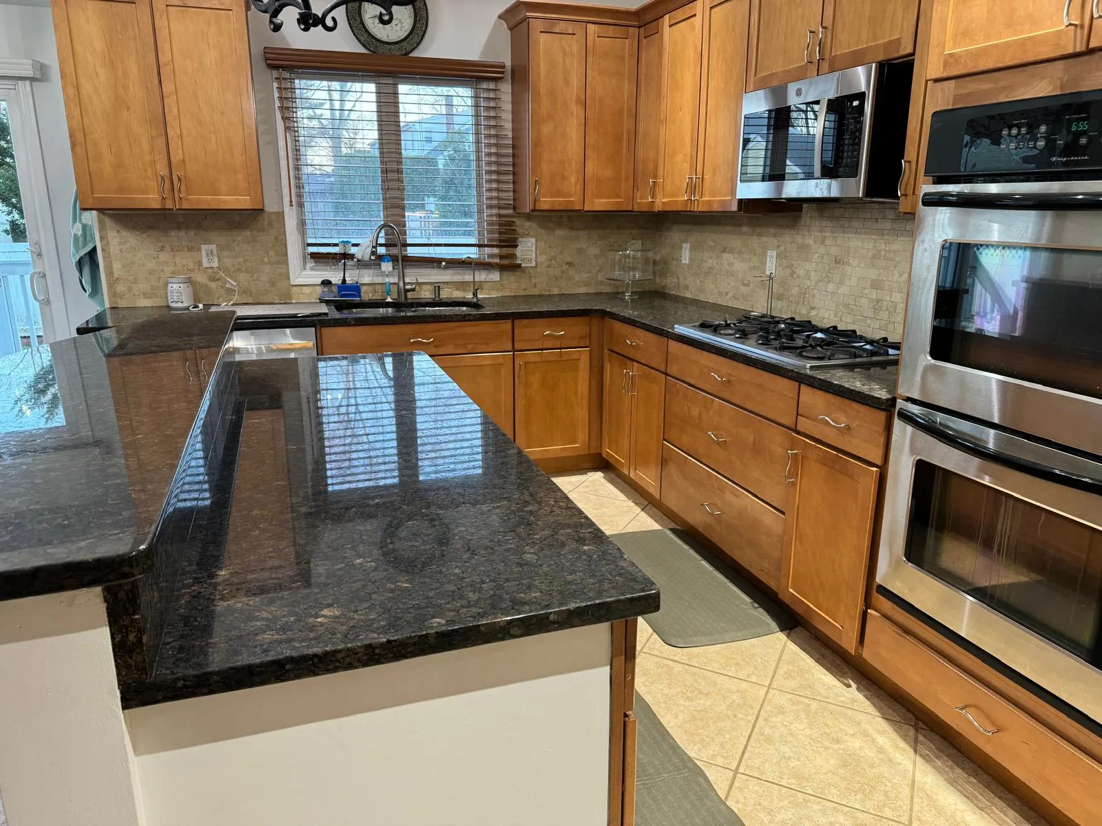 Kitchen/dining room before restyling: from the dining side: granite peninsula, maple cabinets, appliances and odds crowding the counters.