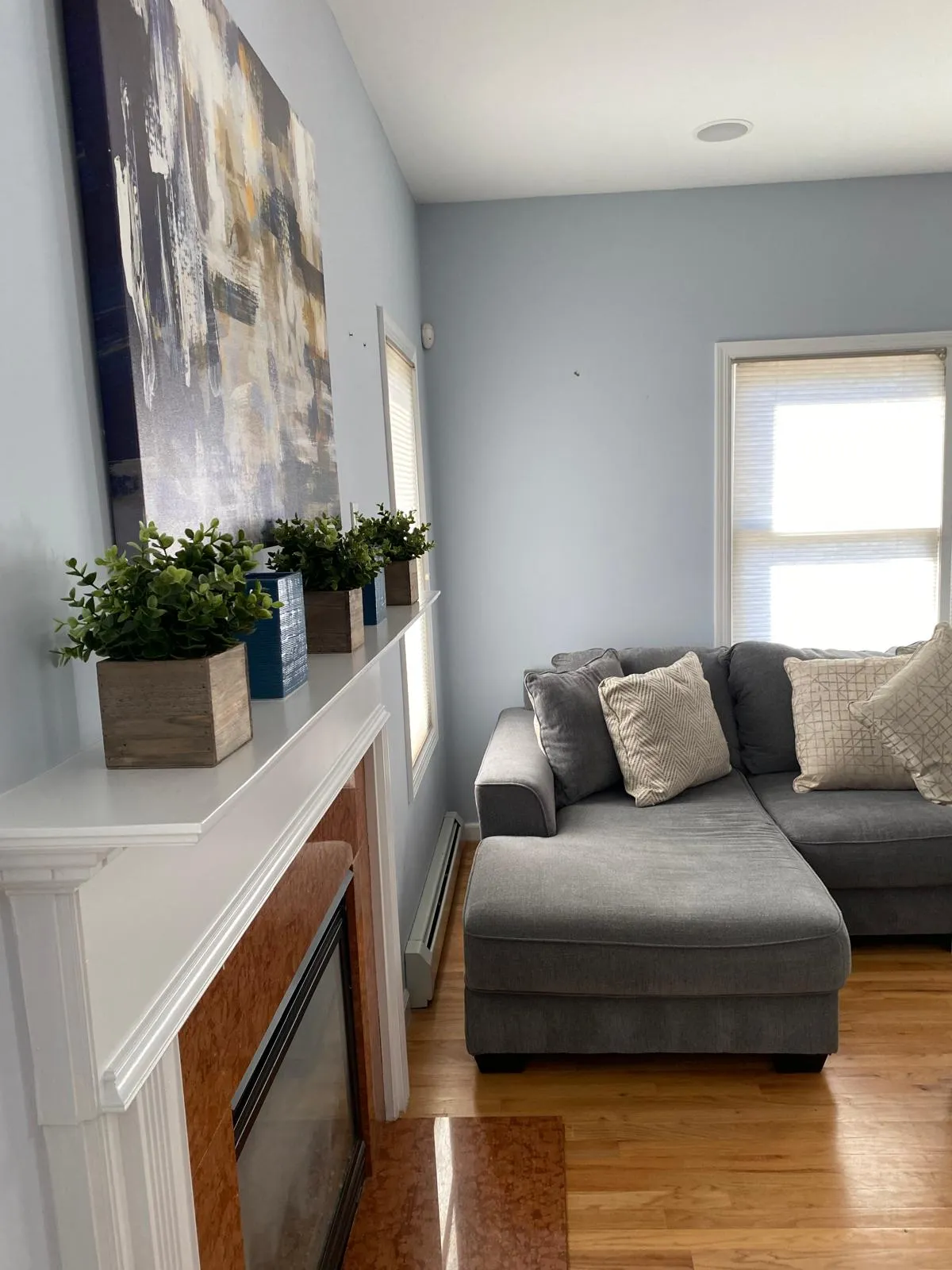 Family room after restyling by Kultur & Decor: mantel detail after: canvas cropped close, four planters stepped along the shelf, chaise and textured pillows alongside.