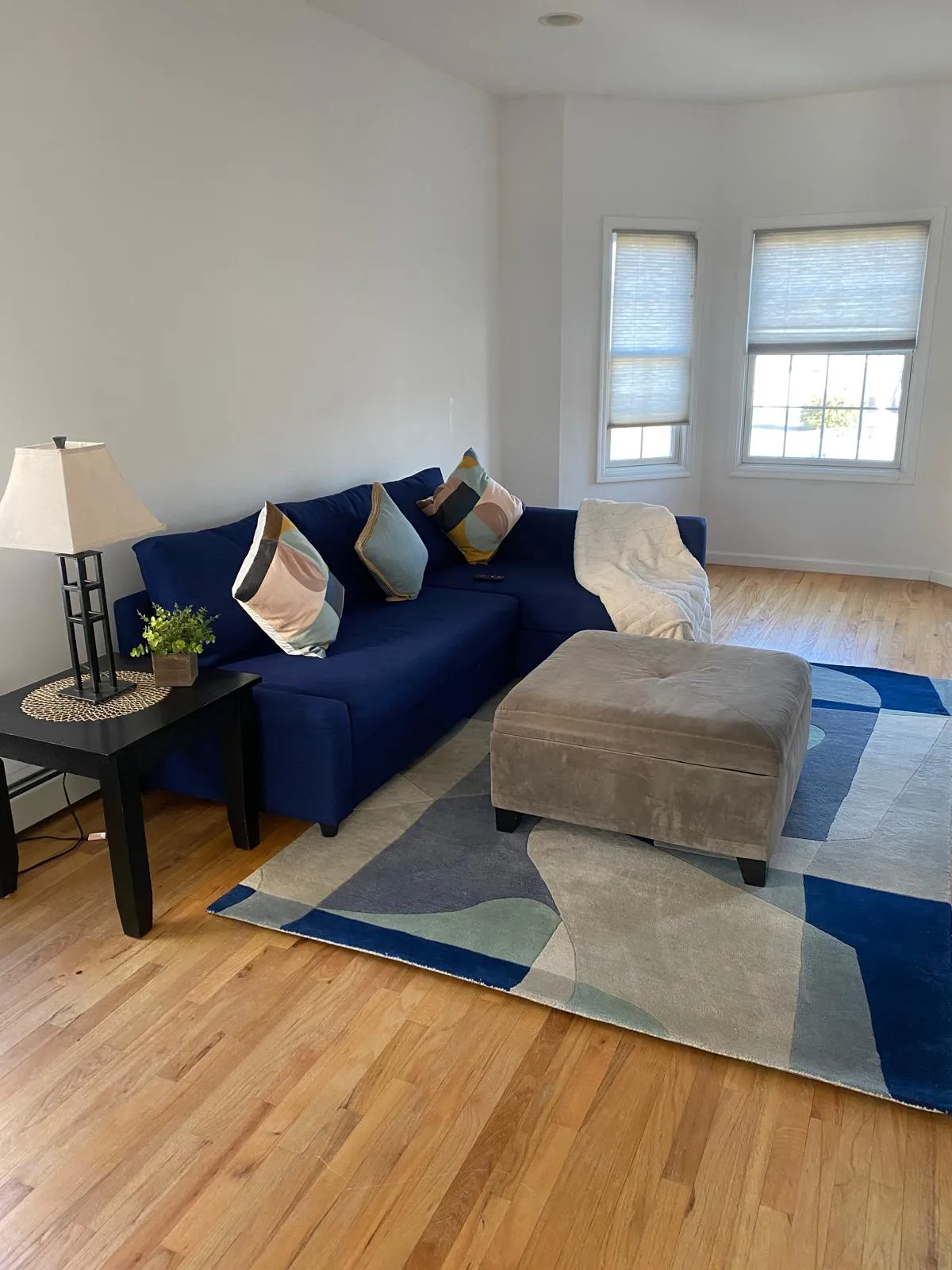 Living room after restyling by Kultur & Decor: navy sofa, geometric blue rug, suede ottoman, corner windows.